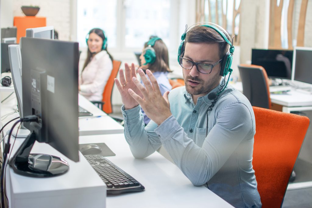 Young handsome male technical support agent trying to explain something to a client while using hands-free headset at call center