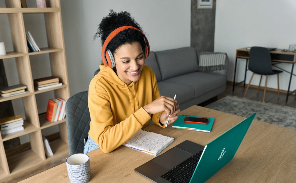 A young smiling adult sitting at home on a laptop completing an online learning course.