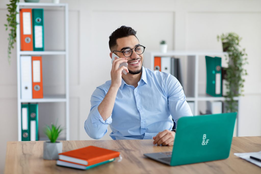 Handsome young man in formal wear talking on smartphone, enjoying conversation at workplace. 